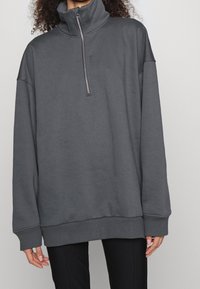 Sweat-shirt zippé gris avec col montant, coupe décontractée et manches longues. Comprend des poignets et un ourlet côtelés avec une texture lisse.