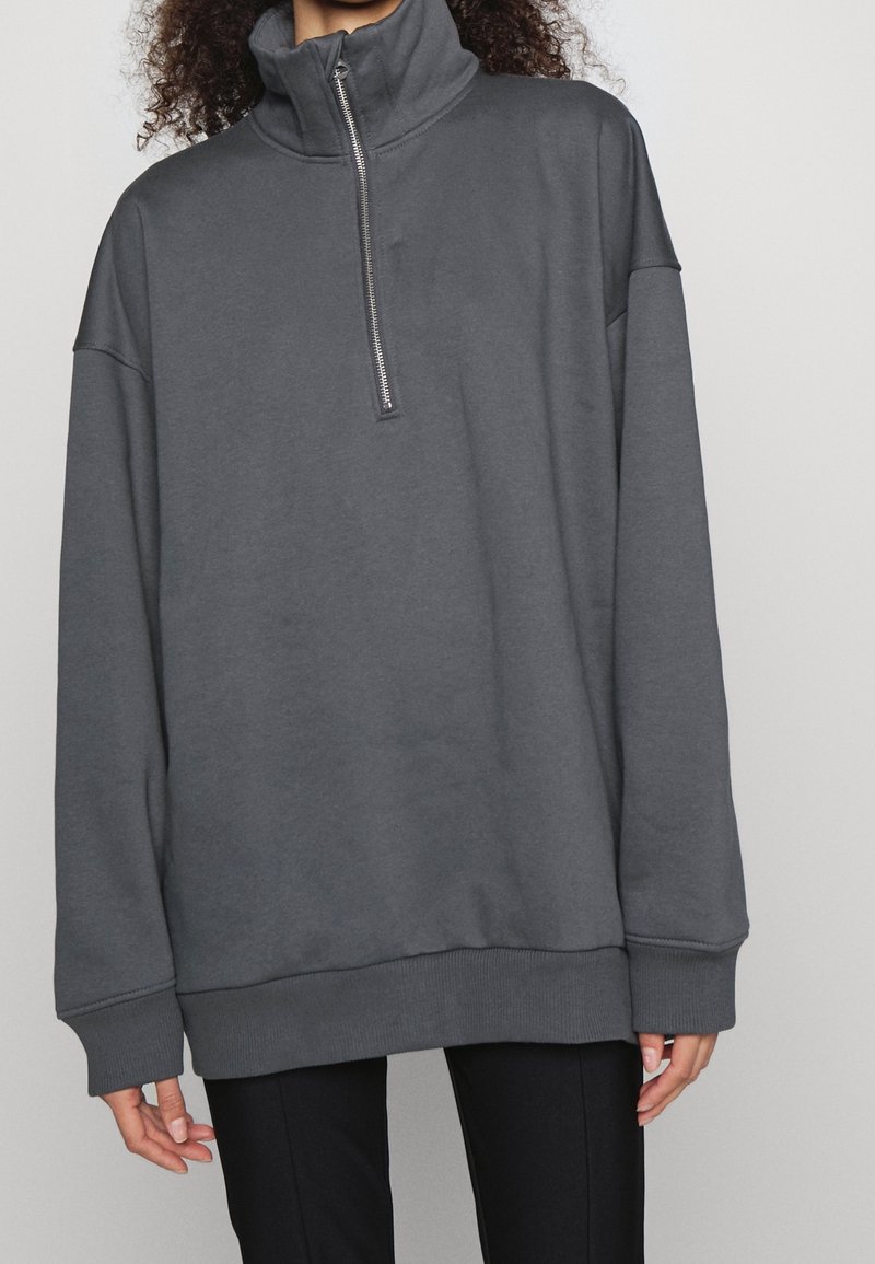 Sweat-shirt zippé gris avec col montant, coupe décontractée et manches longues. Comprend des poignets et un ourlet côtelés avec une texture lisse.