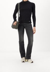Zwarte top met lange mouwen, grijze flared jeans en beige sneakers. Grijze schoudertas met verstelbare riem en zilveren gespen.