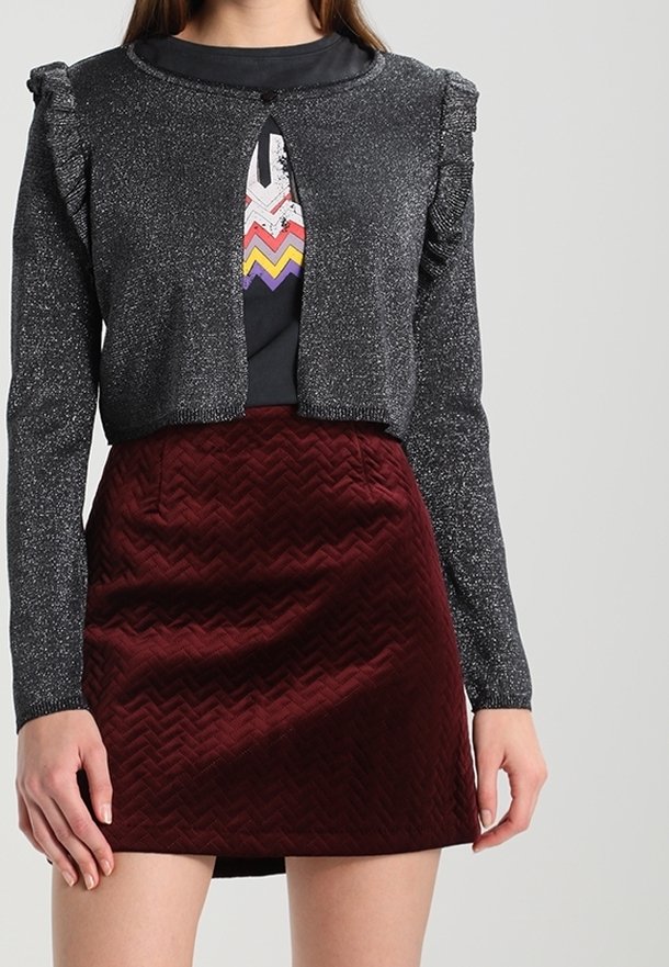Glittrande svart cardigan med volangkanter, som bärs tillsammans med en vinröd kjol med ett chevronmönster. Båda plaggen har en figursydd design.