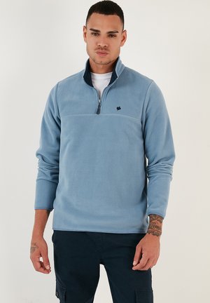 Light blue fleece pullover with a quarter-zip, stand collar, and chest seam. Features a small dark logo on the left chest area.