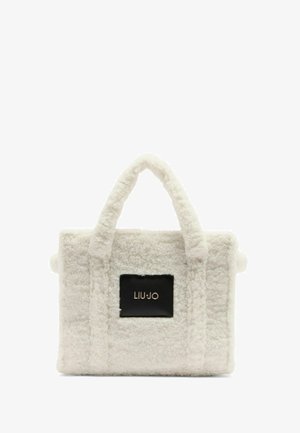 White plush tote bag with textured fabric, two handles, and a black rectangular logo patch. Square shape with soft, fluffy appearance.