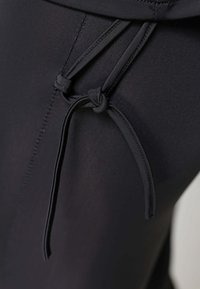 Zwarte stof met een geknoopte trekkoorddetail, gladde textuur en zichtbare stiksels, ontworpen voor een getailleerde uitstraling.