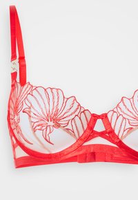 Soutien-gorge en dentelle rouge avec broderie florale sur des sections transparentes, bonnets rembourrés, bretelles réglables et un fermoir décoratif à l'avant.