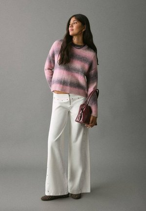 Maglione lavorato a maglia a righe rosa e grigio, pantaloni a gamba larga bianchi a vita alta con borchie e una piccola borsa bordeaux, abbinati a scarpe marroni.