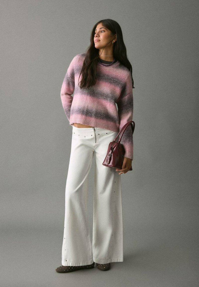 Suéter de punto a rayas rosas y grises, pantalones de tiro alto blancos de pierna ancha con tachuelas, y un pequeño bolso burdeos, combinado con zapatos marrones.