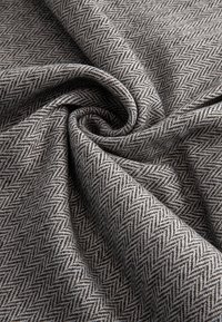 Tissu gris avec un motif chevron densément tissé, plié en spirale, montrant la texture et de fines lignes diagonales.