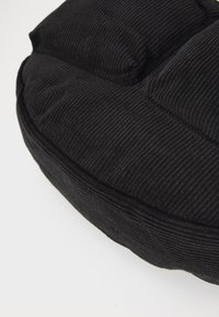 Black corduroy cushion with a round shape, featuring raised sections and a textured surface, stitched edges, and a soft appearance.