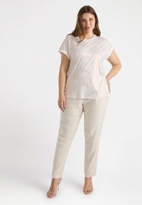 Top de manga corta, de color claro, con un patrón ondulado; combinado con pantalones crema, ajustados; modelo usando sandalias de tacón nude con tiras.