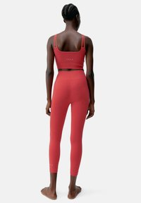 Top corto sportivo rosso con spalline regolabili e leggings a vita alta coordinati, caratterizzati da una finitura testurizzata e un dettaglio con il logo sulla parte posteriore.