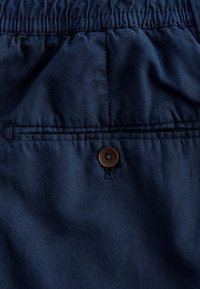 Tecido de culoare bleumarin cu o textură netedă, având un brâu elastic, un singur buzunar la spate și un detaliu cu un buton maro.