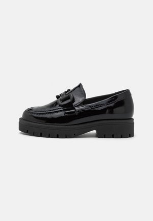 Mocassins en cuir verni noir avec un bout arrondi, une semelle en caoutchouc noir épaisse et des accents décoratifs en métal à l'avant.