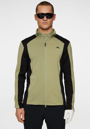 Ljus olivgrön och svart zip-up jacka med hög krage, figursydd form och logotypdetalj. Tillverkad av ett mjukt, stretchigt material.