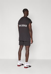 Svart oversized crew neck t-skjorte med "CREW 48" trykt i hvitt på baksiden, sammen med matchende shorts og hvite sportssko.