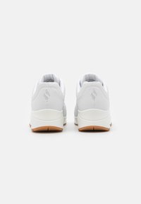 White athletic shoes with a smooth surface, cushioned heel, and gum rubber outsole. Features a subtle logo on the heel and a padded collar.