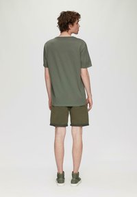 Oliwkowa bawełniana koszulka i szorty, charakteryzujące się luźnym krojem, krótkimi rękawami i podwiniętymi brzegami. Połączone z oliwkowymi trampkami.