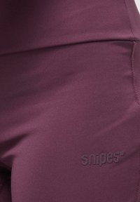 Bordeaux, elastiske leggings laget av glatt stoff; har en tonet "snipes"-logo nær midjen og flatlock-sømmer langs sømmene.