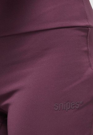 Burgundowe, elastyczne legginsy wykonane z gładkiego materiału; posiadają tonalne logo "snipes" w pobliżu pasa oraz płaskie szwy wzdłuż krawędzi.