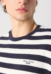 Navy- und weiß gestreiften T-Shirt aus Baumwolle, mit Rundhalsausschnitt und einem kleinen Logo "[Marc O'Polo] DENIM" auf der linken Seite.