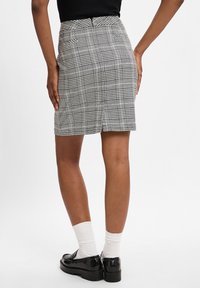 Jupe crayon à carreaux gris avec fente arrière, présentant une coupe ajustée et un tissu texturé. Associée à des mocassins noirs et des chaussettes blanches.