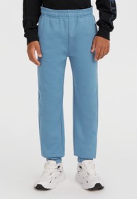 Hellblaue Jogginghose mit elastischem Bund, geraden Beinen und weichem Material, kombiniert mit weißen Turnschuhen.