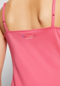 Różowy top na ramiączkach z cienkimi paskami, o gładkiej fakturze i dopasowanym kroju. Nadrukowane kolorowe napisy "This is Love" i "Calvin Klein Jeans".