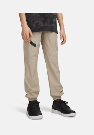 Person wearing beige jogger pants with zippered thigh pocket, black camo shirt, and black sneakers with white soles, standing on white background.