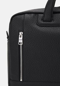 Sac en cuir noir texturé avec un détail de fermeture éclair en métal argenté. Dispose de deux poignées et d'un accent cousu en bas.