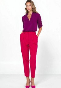 Fuksjowe spodnie o strukturalnym kroju z plisami, zestawione z głęboko fioletową bluzką z dekoltem w serek. Obie odzieże wykonane są z gładkiego, lekkiego materiału.