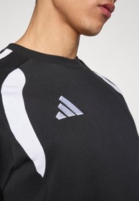 Μαύρο φούτερ με λευκές λεπτομέρειες στους ώμους και ασημί λογότυπο Adidas στο στ ήθος. Λείο υφές και στρογγυλή λαιμόκοψη.