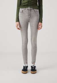 Szürke, skinny farmernadrág, amely illeszkedő kialakítással és diszkrét kopásokkal rendelkezik, fekete sportcipővel, fehér díszítéssel párosítva.