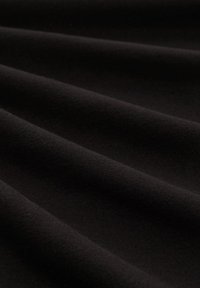Schwarzer Baumwollstoff mit einer glatten Textur, der weiche Falten aufweist, die Wellen bilden und die Flexibilität und das leichte Wesen des Stoffes betonen.