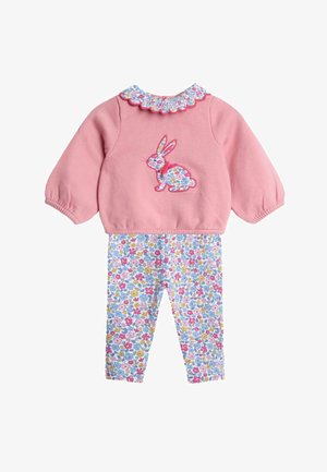 Rózsaszín pulóver virágos, fodros gallérral és nyuszifigura-applikációval; fehér leggings-szel párosítva, amelyek színes virágmintával díszítettek.