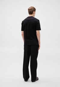 Μαύρο βαμβακερό T-shirt με κοντά μανίκια, επίπεδη λαιμόκοψη; σετ με φαρδιά μαύρη παντελόνια και μαύρα παπούτσια; προβολή από πίσω.