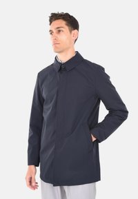 Cappotto impermeabile blu navy con colletto alto, chiusura con bottoni frontali, tasche laterali e taglio diritto, realizzato in materiale tessile liscio.