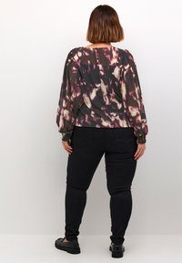 Flowy black and purple patterned blouse with long sleeves and elastic cuffs, paired with black jeans and black flat shoes.
