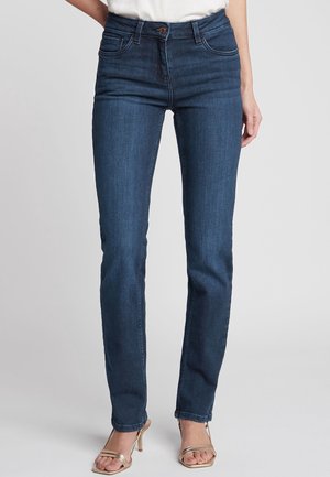 Jean en denim bleu foncé à coupe slim, design à cinq poches, taille mi-haute et texture subtile en rayures. Fermeture par bouton en cuivre à la taille.
