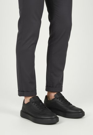 Sneakers nere in pelle con superficie testurizzata, dal profilo basso, design con lacci e suola spessa in gomma, abbinate a pantaloni scuri.