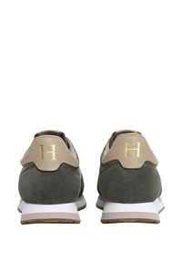 Zapatillas de ante verde con acentos en beige, que presentan un logo dorado con la letra "H" en el talón y una suela de goma blanca. Diseño atlético clásico.