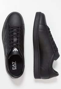 Svarta lädersneakers med en slät yta, rund tå och platt gummisula. Har perforerade detaljer och snörningsdesign.