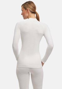 Maglietta atletica bianca a maniche lunghe con un design aderente, tessuto testurizzato e dettagli delle cuciture sottili, parte di un completo coordinato.