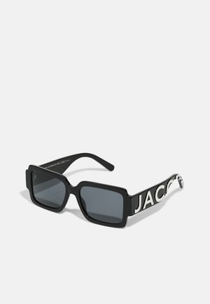 Óculos de sol quadrados pretos com lentes cinzentas. Armação feita de plástico brilhante. Acompanhados por uma haste grossa com a palavra "JACOB" em letras brancas.