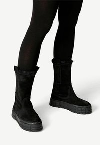 Stivali alla caviglia in suede nero con suola piatta in gomma texturizzata. Presentano un morbido bordo in pelliccia nella parte superiore e dettagli di cuciture laterali.