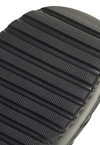 Close-up van een zwarte rubberen zool met gestructureerde groeven en parallelle verhoogde richels voor grip en duurzaamheid.