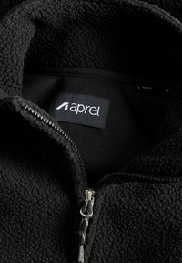 Veste en polaire noire avec un col zippé. Dotée d'un extérieur doux et texturé et d'une étiquette à l'intérieur avec le nom de la marque "aprel."
