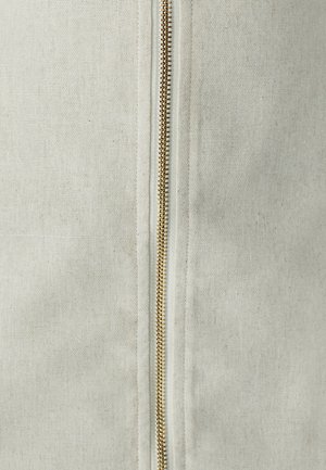 Veste zippée en coton de couleur beige clair, dotée d'une fermeture éclair dorée sur le devant. La texture est lisse avec un motif tissé subtil.
