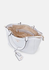 Sac fourre-tout blanc tissé avec doubles poignées, ouvert pour révéler une doublure intérieure beige, une poche zippée et une étiquette suspendue avec un logo de marque doré.