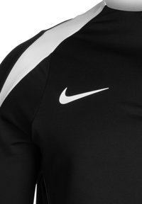 Zwart sportshirt met witte schouderaccenten en een klein wit Nike-logo op de bovenste linkerzijde. Gemaakt van glad, synthetisch materiaal.