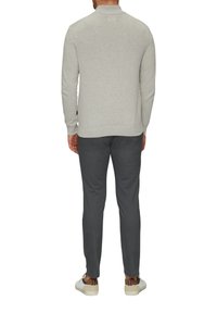 Hellgrauer Pullover mit hohem Kragen, gerippten Ärmelbündchen und Saum, kombiniert mit dunkelgrauen Hosen. Weiße Sneakers mit braunen Akzenten.