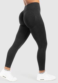 Zwarte high-waisted leggings met een textuurpatroon en gebogen stiksels, gedragen met witte sportsneakers.